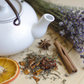 A whie pot of tea with lavender sprigs, 2 petals, cinnamon sticks  and orange peel on a rustic board